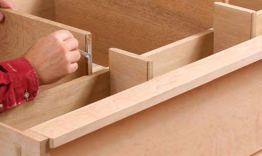 After cutting the dividers to length, use the dovetail bit to cut the keys. A tall fence supports the long boards and a featherboard keeps the piece snug against the fence.
