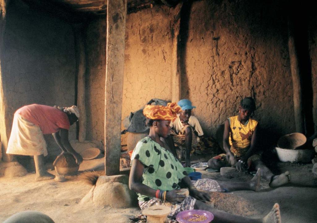 When it has dried to the correct hardness, coils will be added to form the upper portion of the pot and the lip. The other women are making grog. The purple plate contains peanuts for snacking.