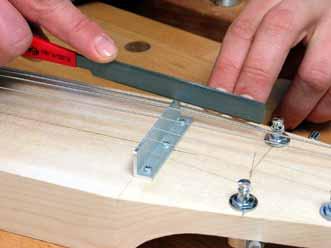 Cutting a notch for a string Cutting the slot with a nut file Putting the strings on Thread the first string through the bridge, stretch it over the nut to the second tuner and bend it there.