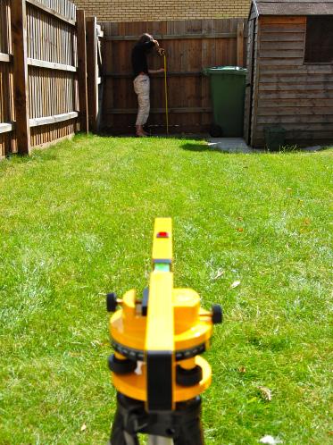 To work out the height of the change of level with a laser level, aim the light beam to the fence or wall at the end of the garden.
