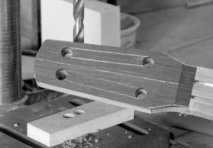 13.43: Here the ends of the slots have been drilled. Use a block below the headstock to prevent the bit from tearing out wood on the underside of the headstock.
