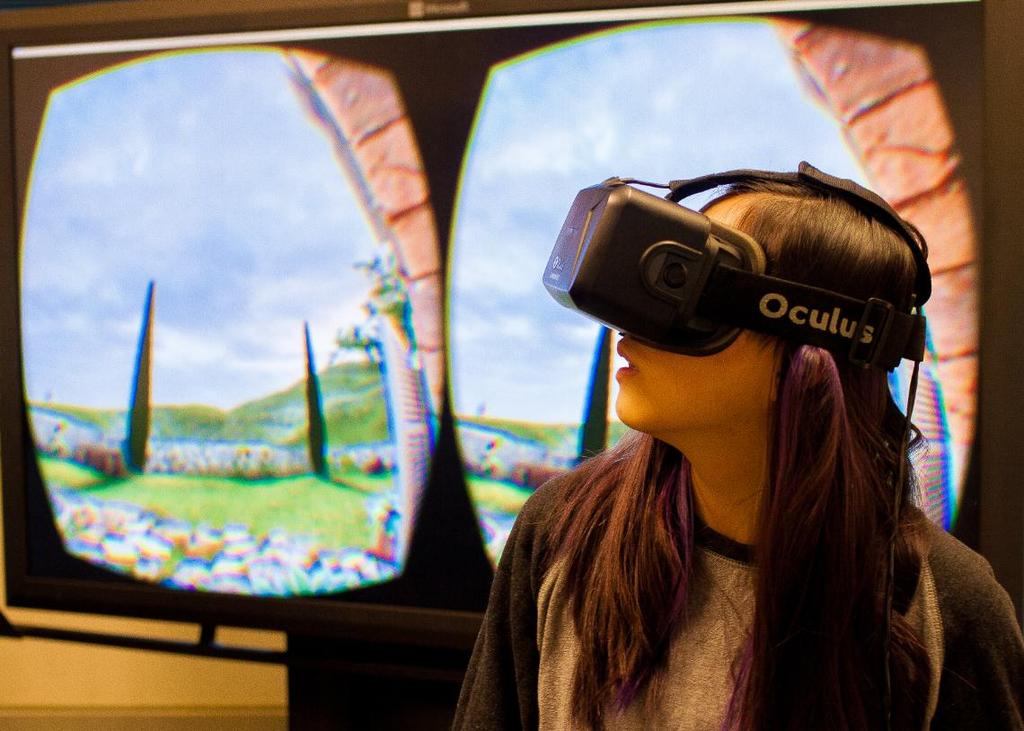 Candice Zhao, a student in the ART 2907 Fall 2015 course, tries Oculus headset goggles. A 2-D version of the immersive 3-D scene is shown on the screen behind her.