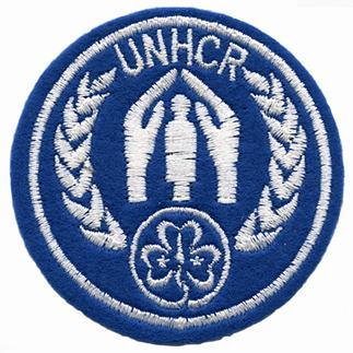 Round; blue; cotton: the WAGGGS Trefoil at the bottom, two wheat sheaves enclosing two hands over a figure of a person, text UNHCR and border all in white