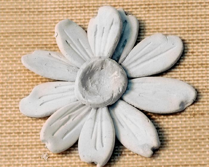 Add a drop of water to the center of the flower to moisten the dry clay, then press a second reserved circle of wet clay onto the front center of the flower.