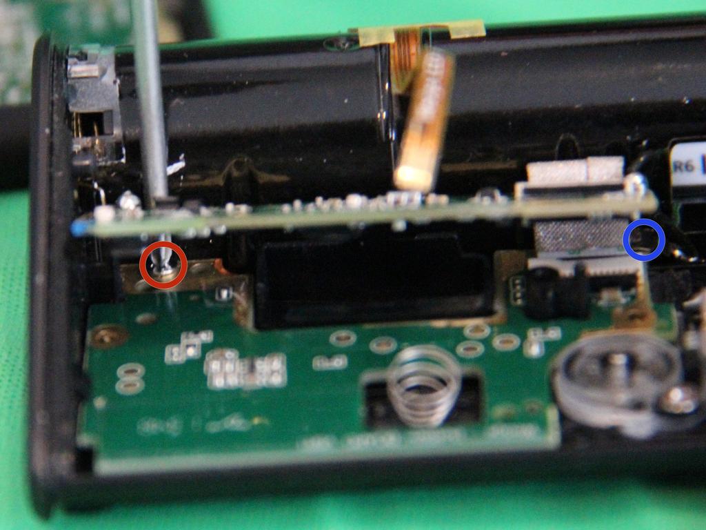 Slide a small phillips screwdriver between the upper PCB and the battery compartment to remove the screw circled in red.