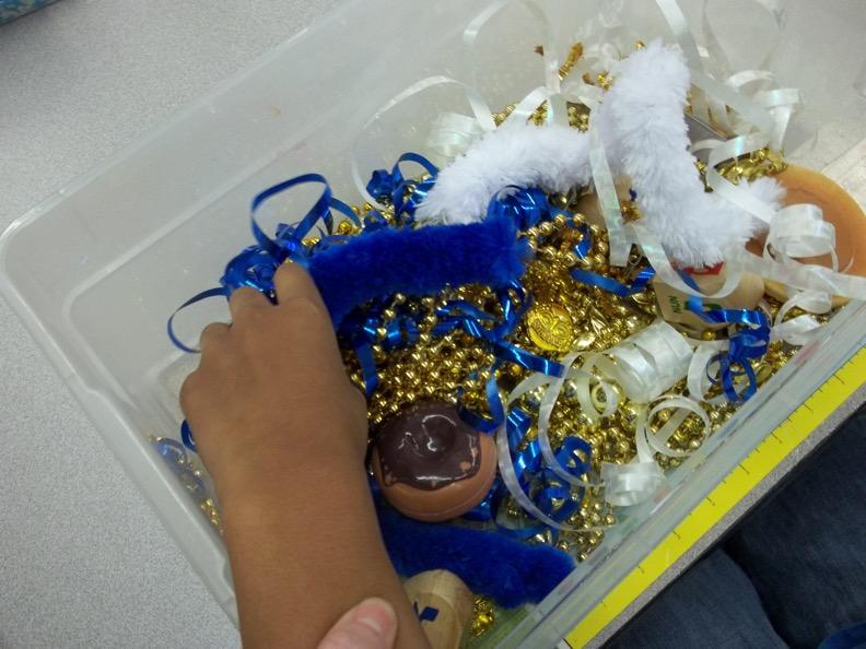 Hanukkah Sensory Ideas Box includes smooth gold bead strings for the gelt, soft big pipe cleaners in the colors of blue and white, small rough gold pipe cleaners, curly white and blue