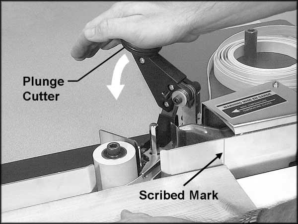 When the trailing end of the workpiece lines up with the scribed mark on the infeed fence, push down on the plunge cutter firmly and rapidly to sever the edge banding material. See Figure 14.