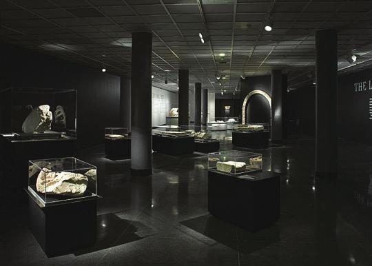 In this room the walls are painted black, dim main lighting with spotlights shining on each vitrine.