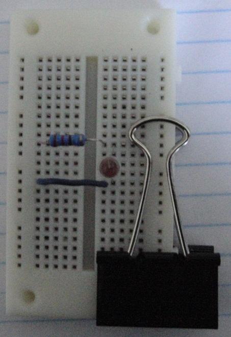 3. Use the solderless breadboard, a 220 ohm resistor, a red LED, the 9V battery, 9V battery clip, and a short piece of hook-up wire (optional) to build the circuit shown in Figure 5.
