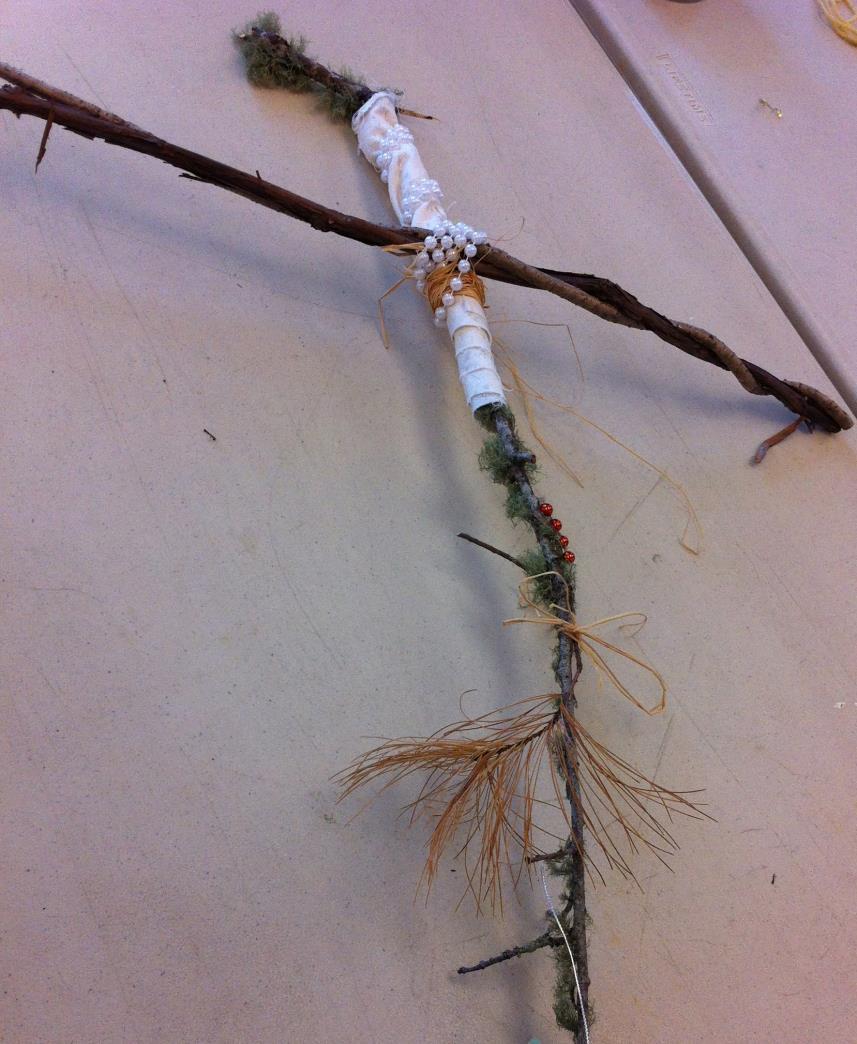 A cross made from sticks, beads, cloth, pine, and moss To me, it represents Jesus suffering