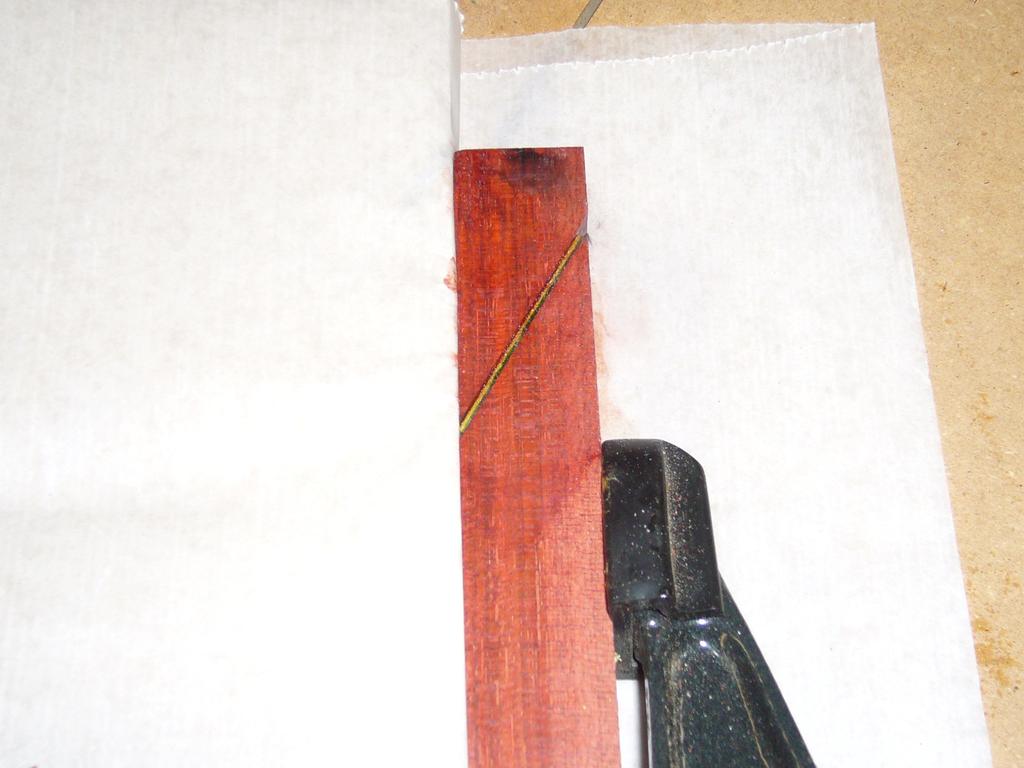 waxed paper under it to keep it from gluing to the sled. I clamp the stock, angled into the straight edge. Apply glue to the bottom side of the veneer and press it to the stock.