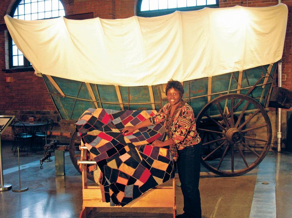 Christine Bethea adjusts her grandmother s crazy quilt that she slept under as her grandmother quilted. It is displayed in front of a Conestoga Wagon circa 1784.