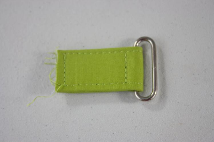 32. Fold one Strap Extender in half so that both raw edges meet, and slide a d-ring/rectangle ring onto the crease.