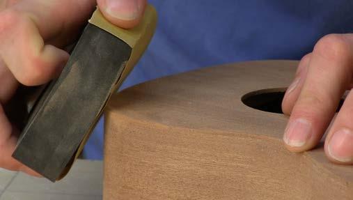 With a straightedge down the middle of the fretboard, find the center point on the tail of the uke. Mark this on a piece of tape. A dowel makes good block for sanding the waist.