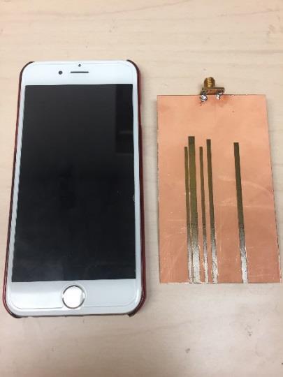 Figure 6.14: Top and bottom views of the fabricated quarter-wavelength slot antenna next to an Apple iphone device.