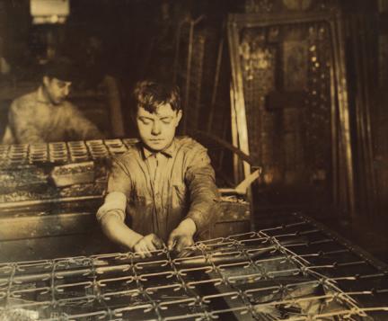 This 1917 photograph shows a 14- year-old boy linking bed springs at a factory in Boston, Massachusetts.