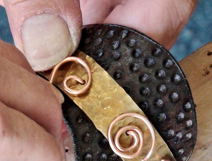 Flatten the midpoint of the wire against the inside of the cuff so it sits flush to the leather. Repeat to thread a second wire through the fifth and sixth holes in the cuff.