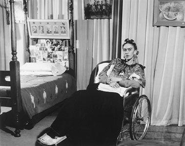 Title: Frida seated in Wheelchair in hospital room with photographs Date of Creation: 1940s Artist/Designer: Lola Álvarez Bravo