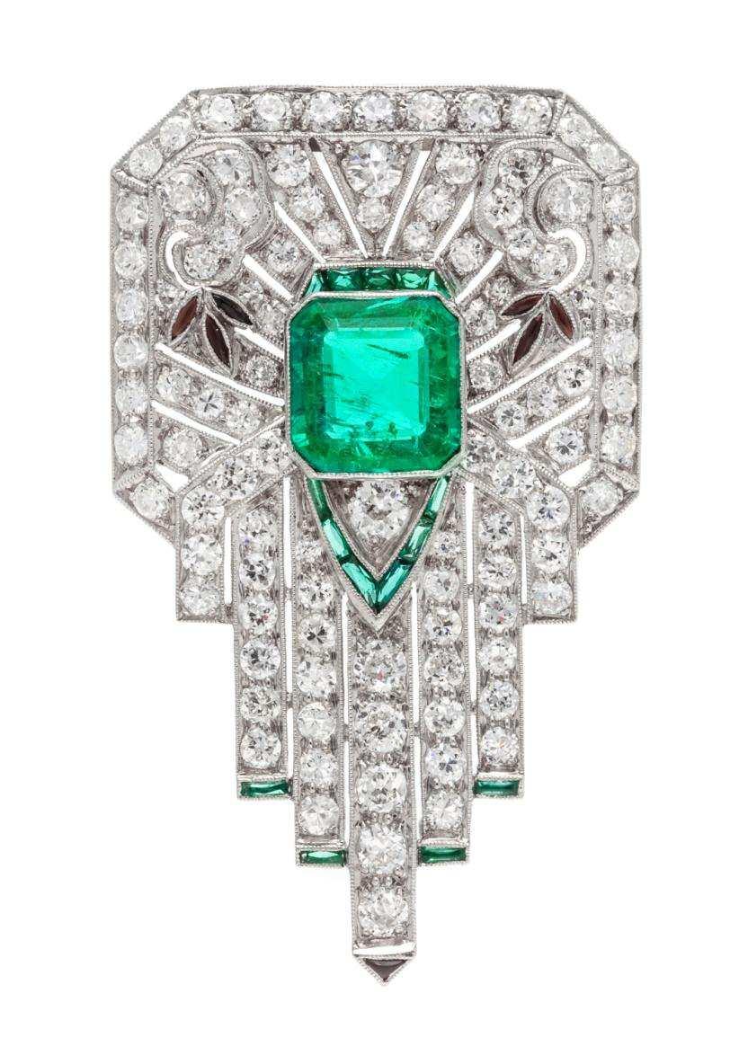 Lot 104 An Art Deco Platinum, Emerald, Diamond, and Multigem Clip Brooch, in a geometric openwork design with millegraine edgework, containing one octagonal step cut emerald measuring approximately 9.