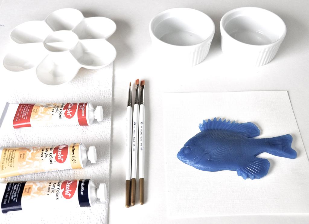 On a tray, bring the paper, newspaper, fish, palette, brushes, jar of water, the paint, and paper towels to a table. Cover a space with newspaper.