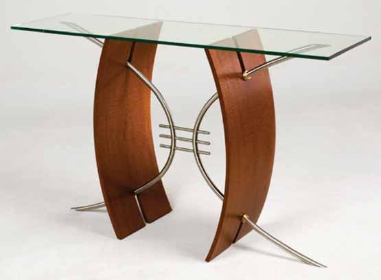 A photograph of a Parabola Hall Table designed by Nathan Hunter is shown. Two curly wood panels intersect steel parabolas to support a glass top. The curved panels are portions of an ellipse.