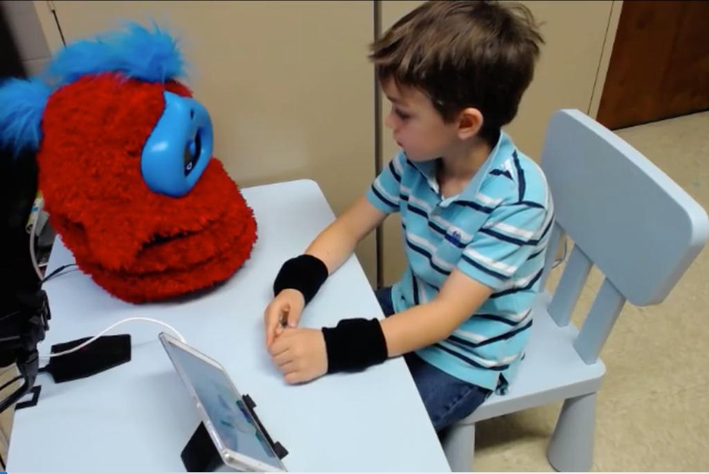 Fig. 1. A child listens to the autonomous robot Tega tell a story during the study. The story pictures are shown on the tablet. C.