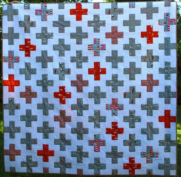 Red Cross What you make: A 58 by 60 simply pieced quilt. The offset cross design makes a stunning quilt. This quilt uses a variety of grey and red fabrics to make the cross blocks.