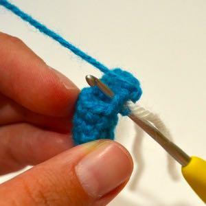 Insert hook in next st, pull up a loop, insert hook into the middle of the side of the flap and pull up a loop, pull yarn through all three