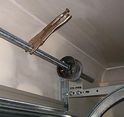 Place vice-grips or a G-clamp in the vertical track on one side above a roller to prevent door from lifting during tensioning.