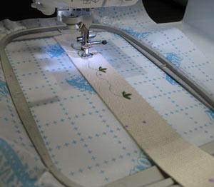 Attach the hoop to the machine, load the design, align the needle over the center point of the strip, and embroider the design.