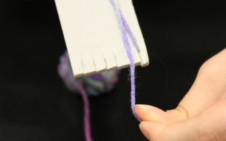 Hold the tail end of the yarn by pressing it into the back of the cardboard loom with