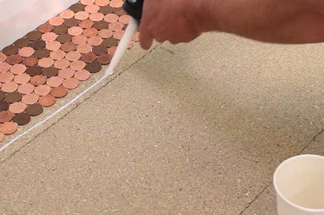 DIY Adhesive Using a sealant gun dispense a thin bead of adhesive along the floor and stick the pennies down - using an adhesive that starts off white and dries clear so you