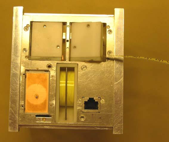 Figure 2. Photo of the nadir surface of the satellite showing S-band patch antenna, VHF and UHF antenna containers, the gravity gradient boom (unfolded) and the RJ-45 connector for ground support.