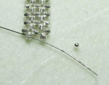 Take the other thread and go through the bottom right spacer towards the left. Put one round bead on the needle.