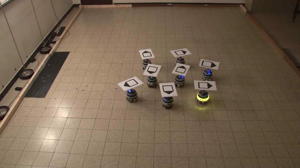 (b) The arena seen from the overhead camera used for tracking: on the left we placed a light source realized by four lamps; a carton hat with a directional marker is placed on each foot-bot robot, in