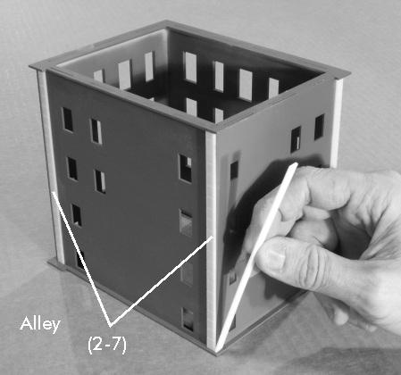 On the alley wall, glue one part (2-7) on the left side up against the overhang of part (2-5) and one part (2-7) to the right side keeping the corner flush.