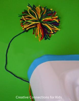 Make a yarn pom-pom Run yarn or string through the top to the bottom and tie, leaving a length of yarn to create the