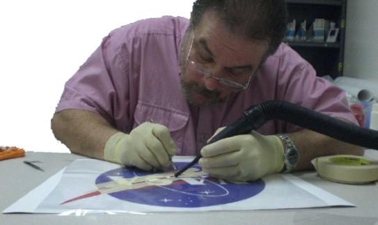 AZ specialist completing final details on NASA logo. AZ scientists work with government agencies, the military and aerospace companies in the application of coatings onto spacecraft hardware.