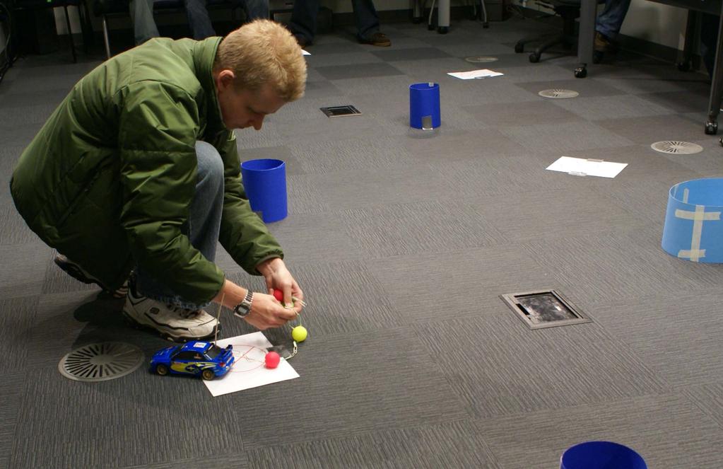 Sammpa, attaching a bomb to the RC car. Taped to the ground in specific locations were pieces of paper marked with a red circle.