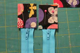 Taking the last two zippers, pin a zipper tab (folded side toward the zipper) in place at