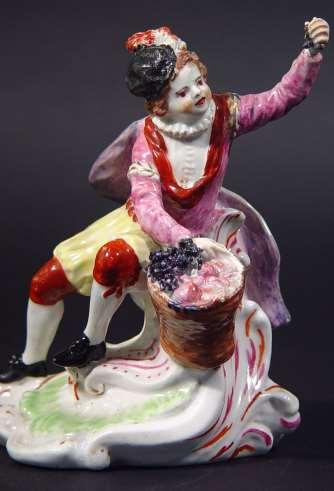 A Vauxhall Porcelain Figure of a Grape Vendor, Circa 1755 The figure is modelled as a youth holding a bunch of grapes in one hand and a basket of fruit in the other.