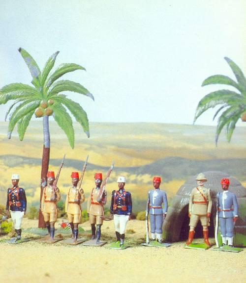 Three figures from Britains set 225 - King's African Rifles surrounded by other native African figures by Britains, depicted in a "native" environment. The photo is taken from Source 7.
