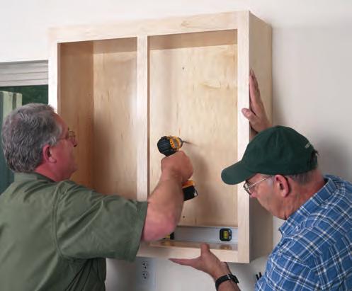 G With the cabinet held to the wall, drive the screws through the clearance holes and into the wall studs using a drill.