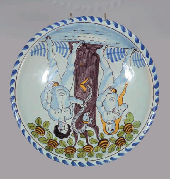 An exceptional English Delft blue dash charger, comically painted in coloured enamels with Adam and Eve flanking the serpent in the apple tree, 12 7 /8"