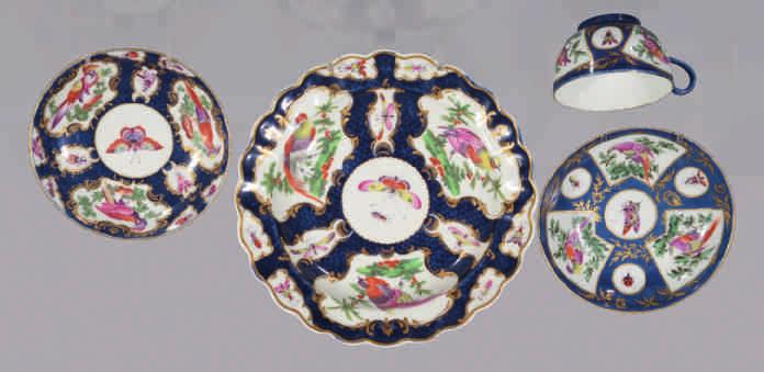 A Worcester teacup and saucer, the cup with loop handle, painted in coloured enamels with exotic birds in branches, within gilt fan shaped panels, and with roundels of insects, on a powder blue