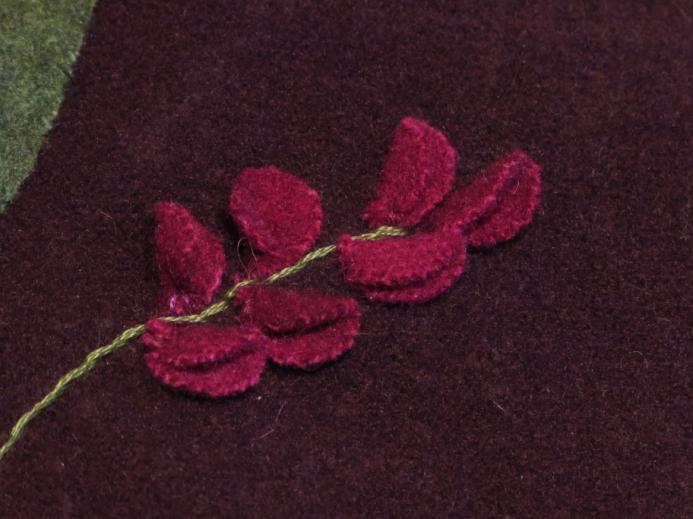 Using two strands of floss, stitch eight straight stitches, each topped by a single French knot (made with two strands of floss), to secure the very small flower piece (E).