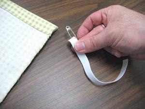 Next, cut two 7 inch pieces of elastic. Attach a safety pin to one end of one of the pieces of elastic.