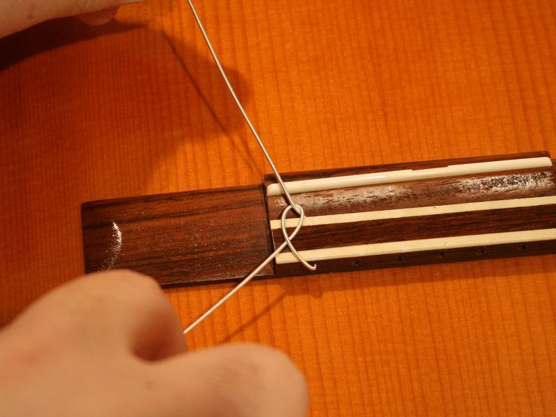 Insert the thick end of the string into the top of the bridge and thread it through until about 3 to 4 inches of the string
