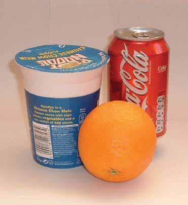 photograph of some of the contents of a child's lunch box shows a Coke can, a Pot Noodles pot and an orange which are in contact with each other.