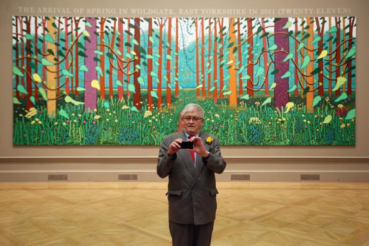 British artist David Hockney takes a picture of press photographers with his mobile phone as he poses in front of his painting entitled "The Arrival of Spring in Woldgate, East Yorkshire in 2011" at
